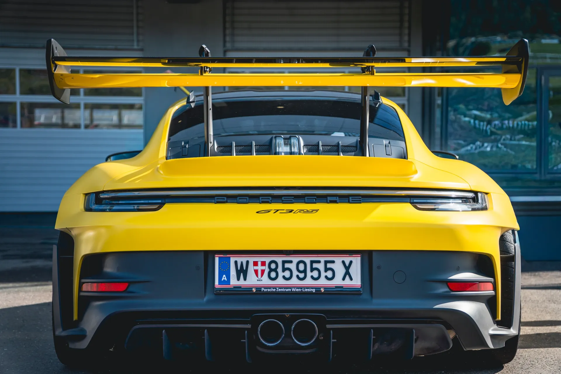   Rear view of a yellow Porsche 911 GT3 RS showing its large rear wing, twin central exhausts and diffuser.