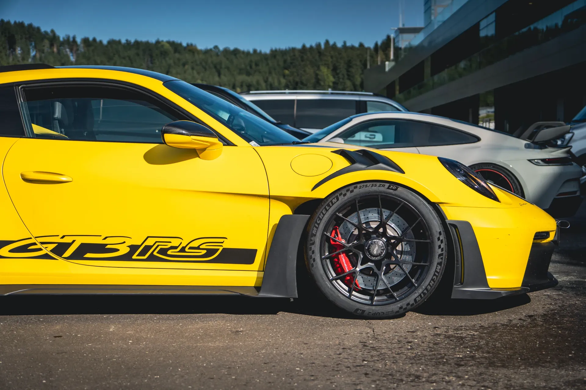 Close-up of a yellow Porsche 911 GT3 RS showing its front wheel, red brake caliper, fender vents and black side graphics.