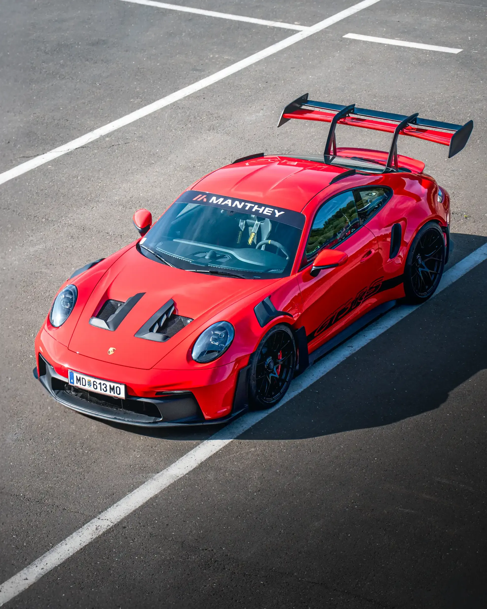 Elevated view of a red Porsche 911 GT3 RS with Manthey windshield branding and a large rear wing at the Red Bull Ring.