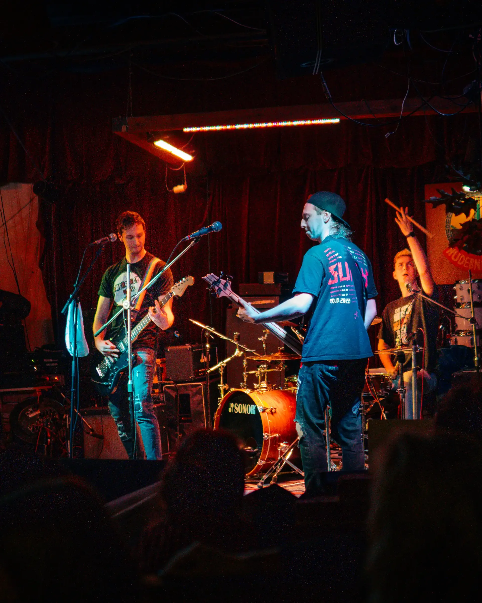 Czech punk rock band Emergency Brake performs on a small club stage as the drummer raises a drumstick.