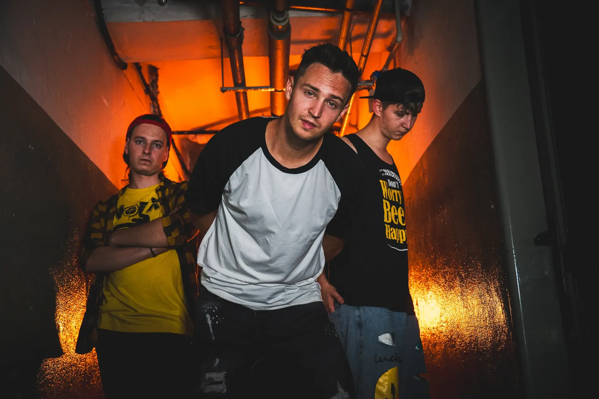 Emergency Brake band portrait in an orange-lit corridor, with the central member leaning toward the camera.