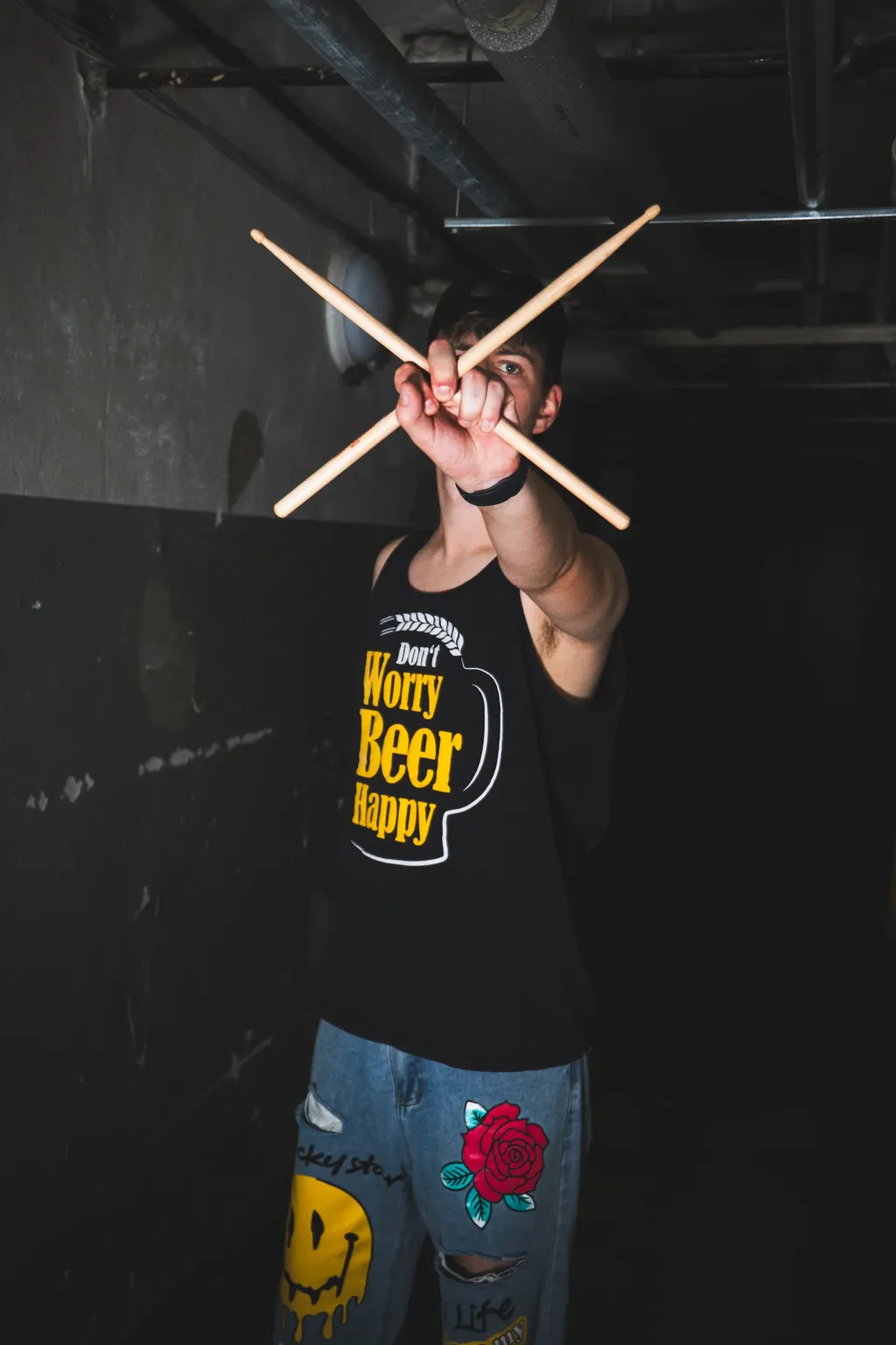 Emergency Brake’s drummer holds crossed drumsticks toward the camera in a dim industrial corridor.